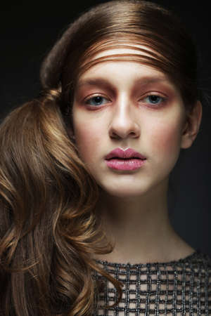 Beautiful woman with make up in pink tones. Girl model with braided braid over black background. Hairstyle in the trend. Beauty, fashion, cosmetics and cosmetology.の写真素材