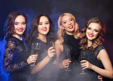 party and people concept - young women clinking flutes with sparkling wine over dark background.の写真素材