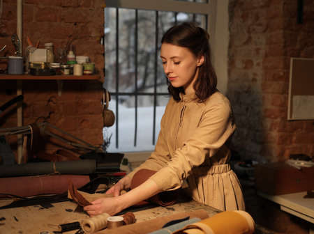 young woman works in a workshop, sews leather bagsの写真素材