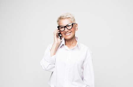 happy old woman with short hair and glasses using smartphone over grey background.