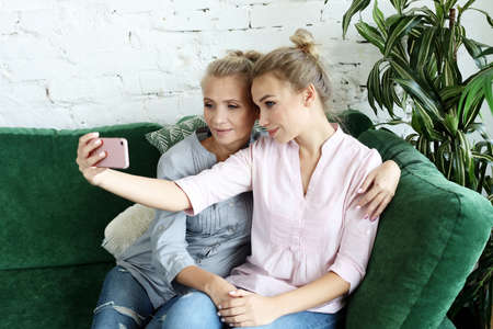 Portrait of beautiful mature mother and her daughter making a selfie using smart phone and smiling,...