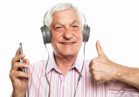Handsome old man in casual wear and headphones is listening to music using a mobile and smiling, show ok sign, on white backgroundの写真素材