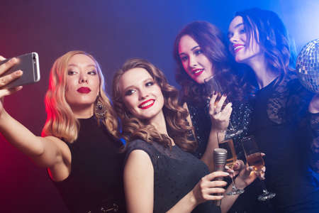 young women in luxury black dresses drinking champagne and having fun with karaoke, selfie and happy time.の写真素材
