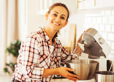 Young woman pastry chef puts ingredients in a mixer, whips cream, dough, makes cake or muffins.