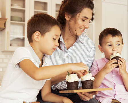 Happy family in the kitchen. Mom and two little boys, brothers, are eating homemade cupcakes.の写真素材