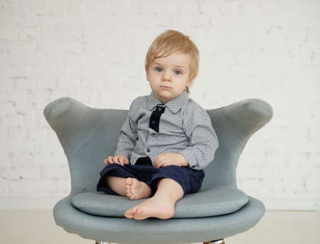 A little boy sitting on a blue chair. The child is bored and looks around.