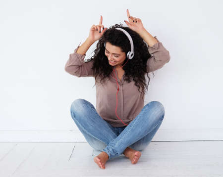 African female listening to her music from her phone with her headphones, sitting on the floor at home.の写真素材