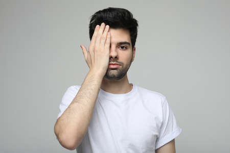 young brunette man wearing casual white t-shirt covering one eye with hand