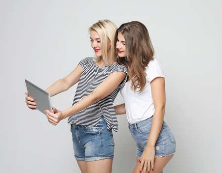 technology, friendship and people concept - two smiling young women with tablet pc over grey...