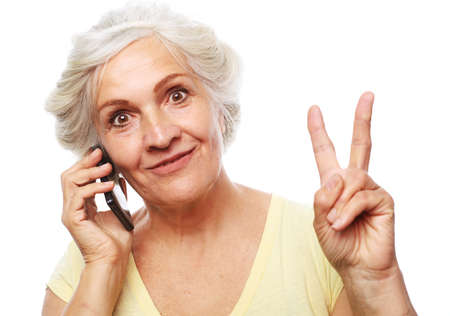 Photo of crazy ecstatic old woman use smartphone and show victory sign isolated over white...