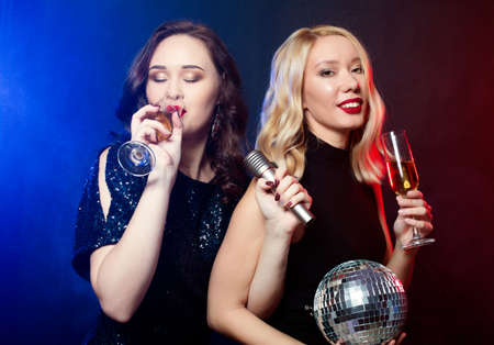 lifestyle, party and people concept: two beautiful young women with wine glasses and microphoneの写真素材