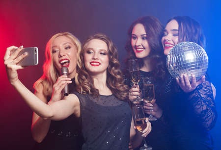 Close-up shot of a group of laughing women wearing black dresses having a party, take selfie with a smartphone. party concept.の写真素材