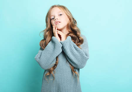 Adorable little girl with long curly blond hair posing on a blue background, close upの写真素材