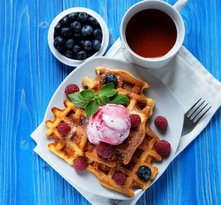 Belgian waffles with fresh berries and ice cream over blue wooden background