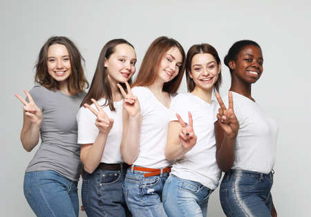 Portrait of five young multiracial women standing together, show victory sign and smiling at cameraの写真素材