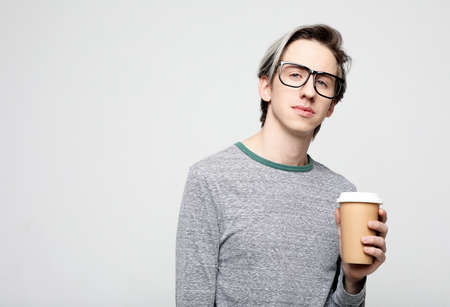 Young man standing with takeaway coffee, happy carefree handsome guy in eyewearの写真素材