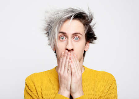 A young handsome man dressed in yellow hoody covers his mouth with his palms.の写真素材