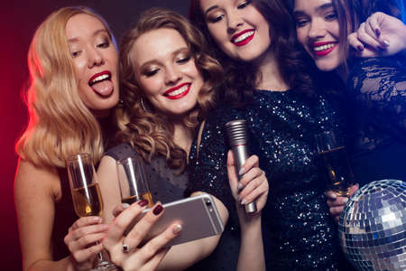 Group of glamour women in luxury black dresses drinking champagne and having fun with karaoke, selfie time.の写真素材