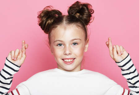 lifestyle and childhood concept: little girl smiles and crosses her fingers, a symbol of hope over pink backgroundの写真素材