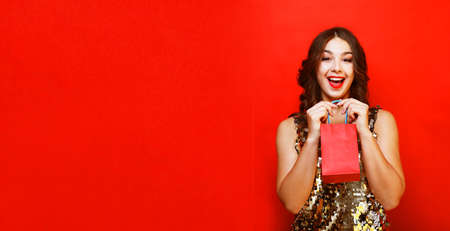 Beautiful young woman holding a red gift bag, anticipation of surprise, joy and happiness