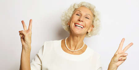 Old people, modern lifestyle, body language concept. Adorable mature wrinkled woman smiles broadly and gives peace sign, enjoys cool nice day.の写真素材