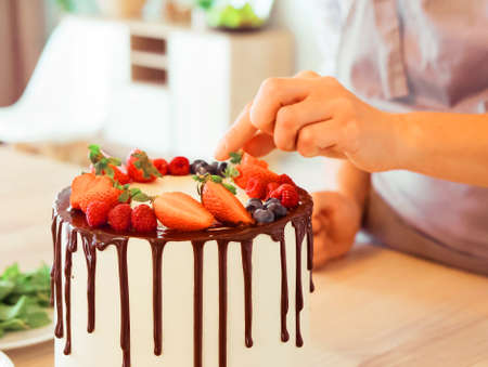 Lifestyle, people, cooking and freelancing concept: close up female hands decorate the cake with chocolate and berriesの写真素材