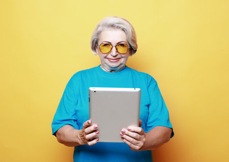 Photo of old attractive lady use tablet isolated over yellow background
