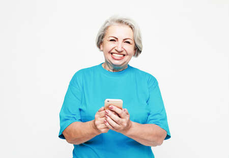 Tehnology and old people concept: Pretty senior female in casual outfit using modern smartphone and...