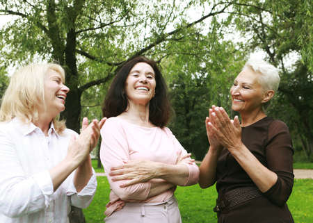 Women friends in the park celebrate a birthday. Clap your hands, congratulations, rejoice. happy summer day. The concept of friendship, happy old age and emotions.の写真素材