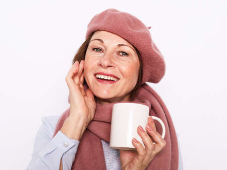 Portrait of senior woman wearing pink hat and scarf with cup of coffee over white background