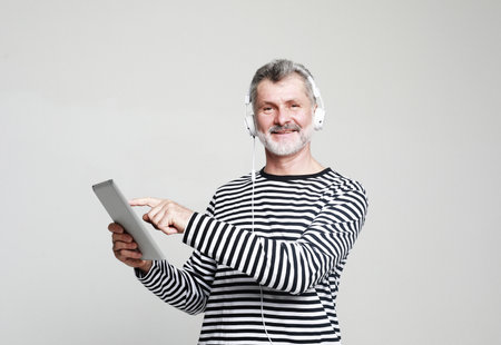 Cheerful senior man listening favorite tracks, isolated on gray background. Joyful male wearing...