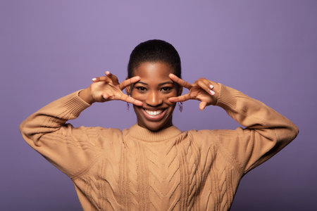 Young African American woman wearing beige casual sweater showing v-sign near eyesの写真素材