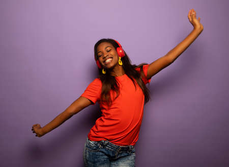 Enthusiastic mix race woman with long hair listening favorite music by headphones and dancing over...