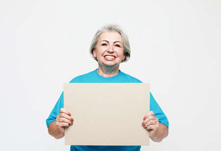 Lifestyle, emotion and old people concept: Portrait of happy senior woman wearing blue tshirt with blank advertising board or copy space over white backgroundの写真素材