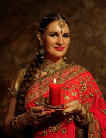 Charming young woman holding a candle. Traditional Indian wedding sari and jewelry.の写真素材