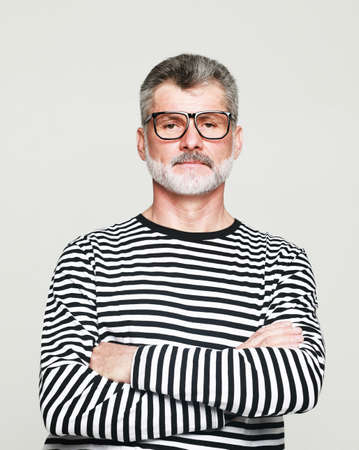 Portrait of senior elderly caucasian old man wearing striped sweater and eyeglasses with arm crossed...