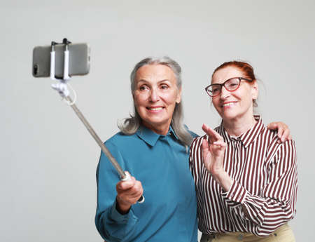 Two elderly women taking a selfie with a stick isolated on grey backgroundの写真素材