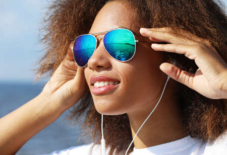 Charming amazing afro american young woman in sunglasses listening to music in headphones on her...