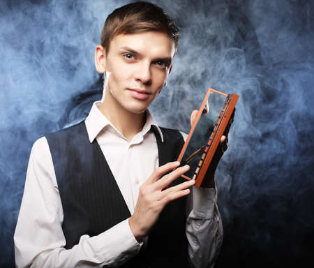 Young male make up artist holding shadow palette and brush over dark smoked background.