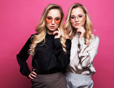 Fashion and beauty concept: Two beautiful young women in casual clothes posing over pink color background. Fashion spring summer photo, nice hair, big smile. Friendship. Two sisters.の写真素材
