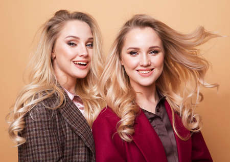 Fashion and beauty concept: Two beautiful young women in casual clothes posing over beige background. Fashion spring summer photo, nice hair, big smile. Friendship. Two sisters.の写真素材