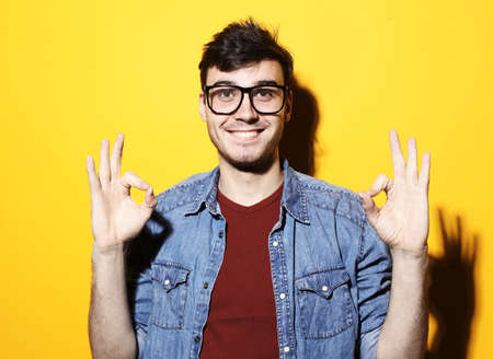 Portrait of handsome excited man in basic clothing smiling and showing ok sign at camera isolated over yellow backgroundの写真素材