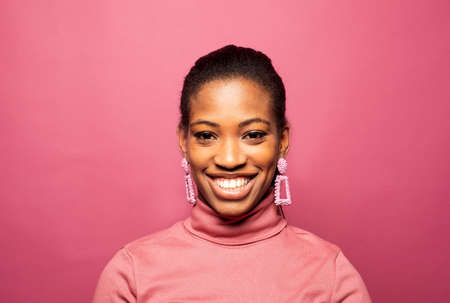 Portrait of young beautiful smiling dark skinned woman smiling and feel happy emotion isolated over pink background.の写真素材