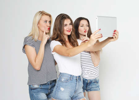 Three young female friends taking selfie with digital tablet, studio shotの写真素材