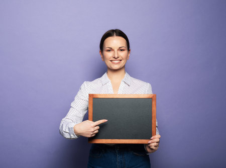 Young smiling woman holding a chalkboard isolated on purple background.の写真素材