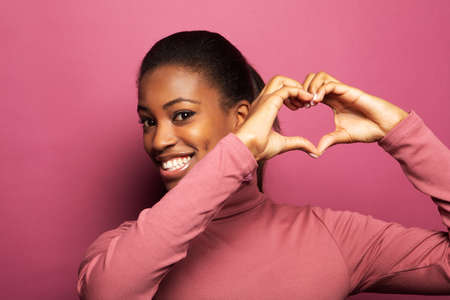 Young beautiful African American afro woman smiling in love doing heart symbol shape with hands over...