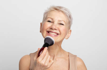 Beauty portrait mature woman applying blush with a makeup brush over gray background.の写真素材