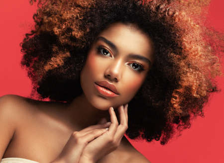 Young beautiful african american woman with afro hair. Glamor makeup. Portrait over Red Background.の写真素材