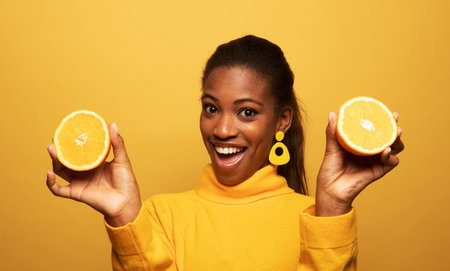 lifestyle, food, diet and people concept: Photo of young afro american woman hold orange slices look amazed isolated on yellow color background.の写真素材