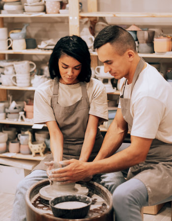 Couple in love working together on potter wheel in craft studio workshop. Lifestyle cocnept.